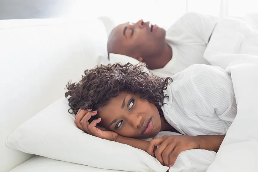 Annoyed wife lays wide awake next to her husband who is snoring loudly in bed