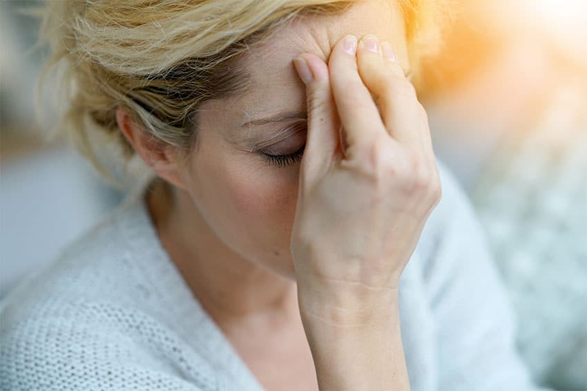 woman pinching her forehead due to a migraine headache