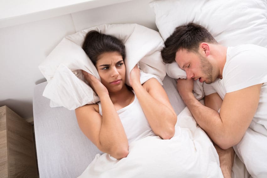 woman plugging her ears while man snores next to her