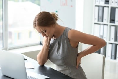 Woman sitting at laptop with shoulder and lower back pain