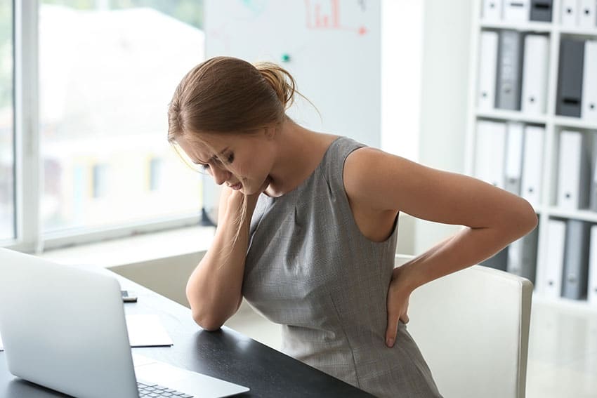 Woman sitting at her laptop with neck and lower back pain