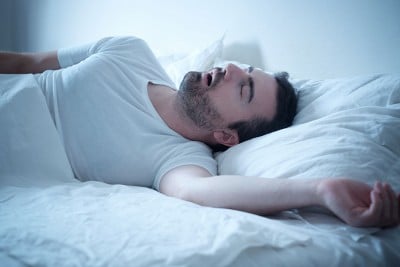 man laying in bed snoring, illuminated by a blue light