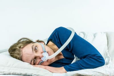 woman with CPAP masks lays uncomfortably on her side