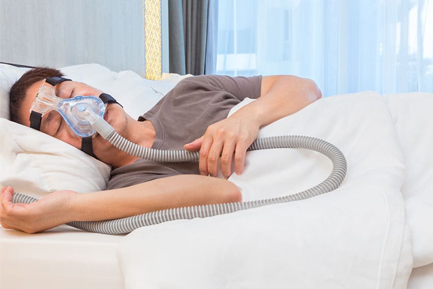 man laying in bed with CPAP mask on to help treat sleep apnea