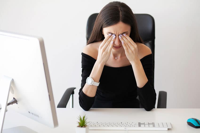 woman sitting at desk holding her face