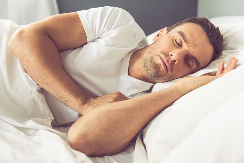 man sleeping peacefully in bed with white sheets