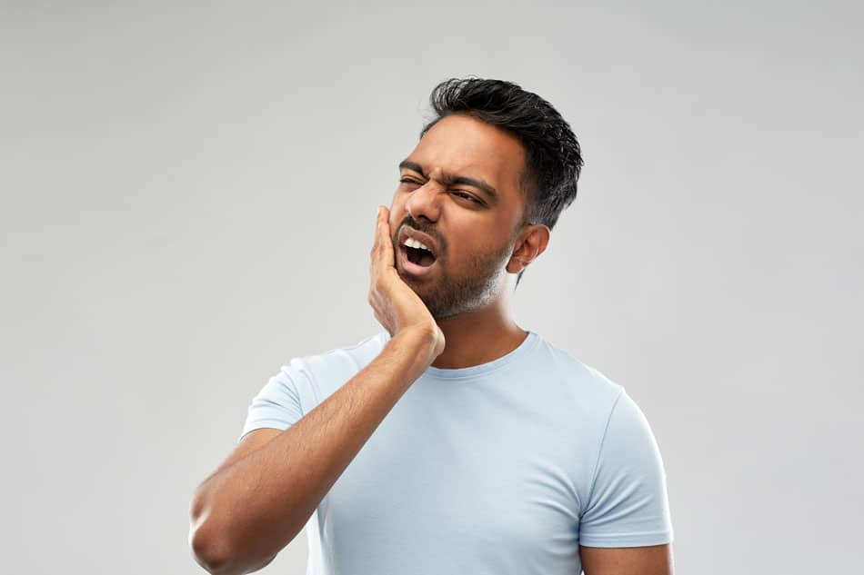 jaw-popping-clicking-detroit Person holding their jaw in pain, illustrating symptoms of TMJ disorder or toothache.