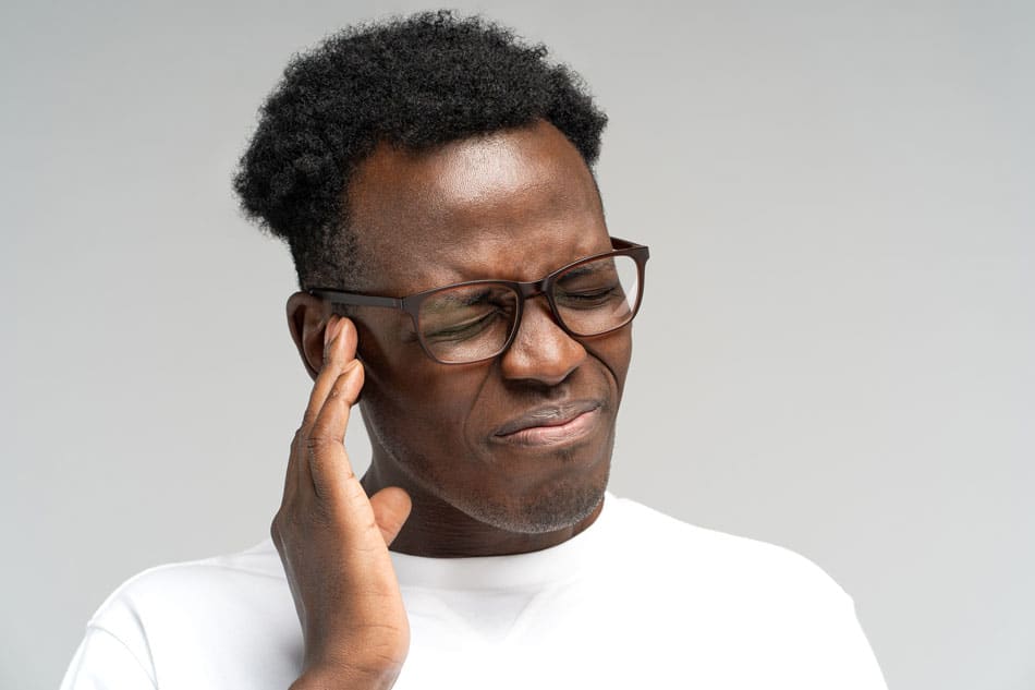 tinnitus-detroit Man holding his temple with a pained expression, illustrating headache, facial pain, or TMJ-related tension.