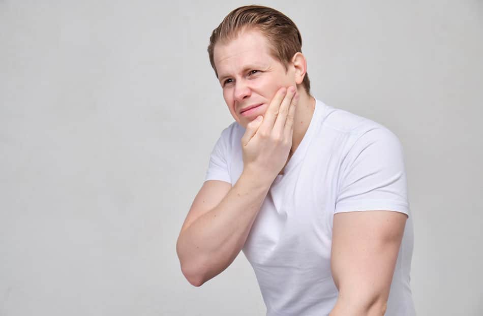 young adult man holding his jaw in pain