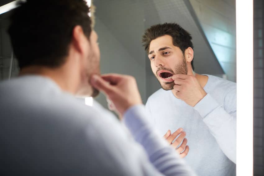 tooth-damage-find-the-cause Man examining his jaw in a mirror, illustrating TMJ symptoms, jaw pain, or limited jaw movement.