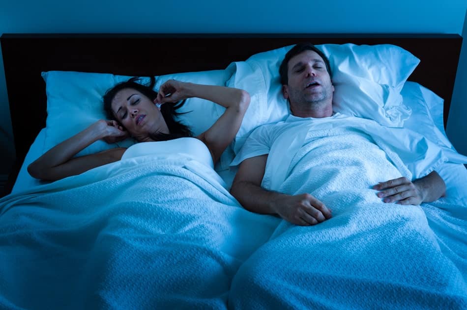 epworth-sleepiness-scale-min Man snoring beside a sleeping partner, illustrating sleep apnea, snoring, and disrupted sleep.