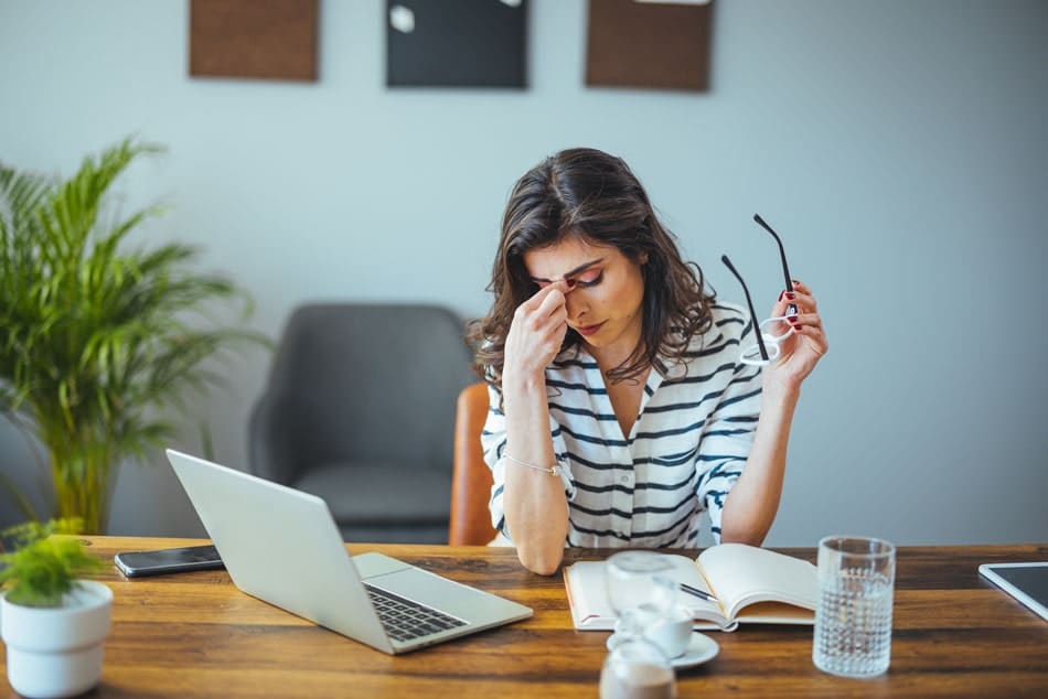 headaches-detroit Woman at desk rubbing her forehead, illustrating headache, fatigue, or TMJ-related facial tension.