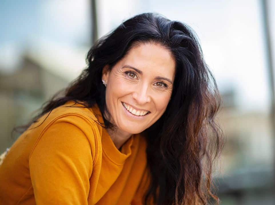 Woman with long, dark hair wearing yellow shirt smiling