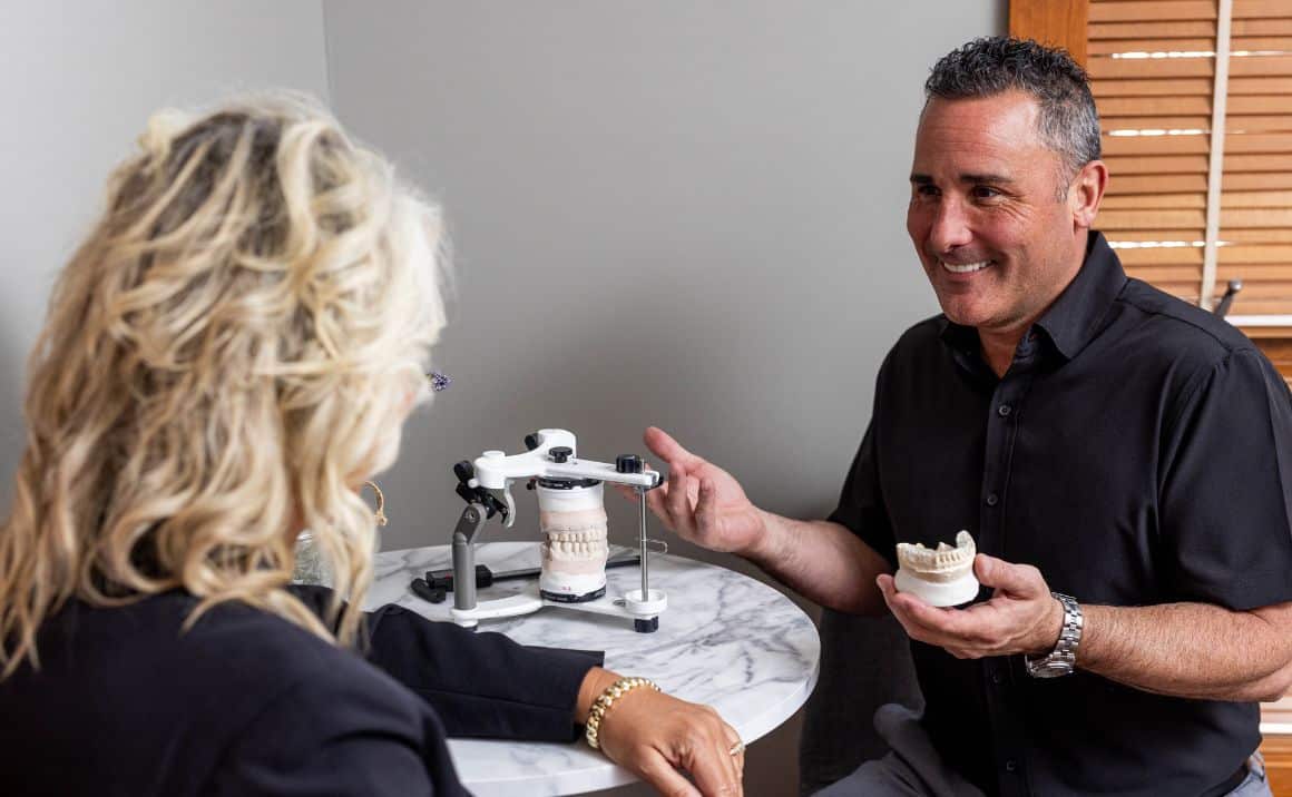 About page content image 3 Dr. Haddad discussing TMJ treatment options with a patient using dental models and jaw alignment tools.
