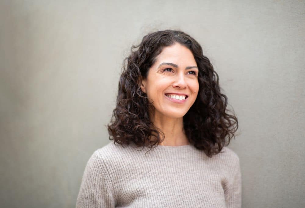 Smiling woman with curly hair, representing comfort and relief after TMJ or sleep treatment.