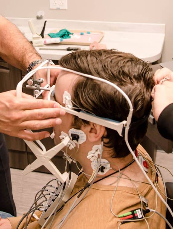Service page image stack 2 Patient undergoing computerized TMJ evaluation with jaw-tracking sensors and diagnostic equipment.