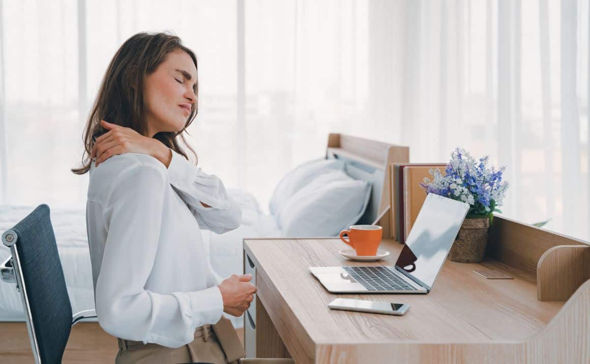 Woman at desk rubbing her neck, illustrating TMJ-related neck pain or discomfort during daily activities.